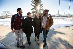 Four international students walking on a bright winter day, laughing.