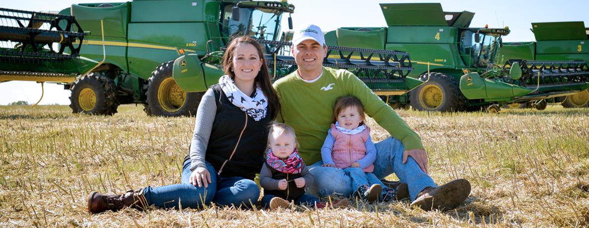 Family sitting in field in front of farm equipment