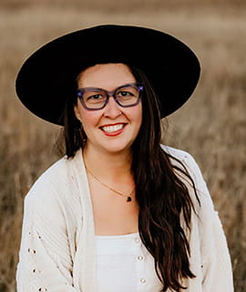 Portrait of Stacey Domolewski, Research and Innovation Coordinator for the Beef Cattle Research Council wearing a black hat and white dress. In the background is a brown field.