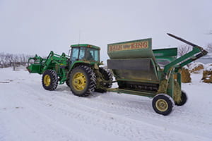 A green tractor attached to a bale-processor hauls feed to be shredded on a snow-covered field in Saskatchewan.
