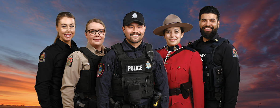 A correctional officer, conservation officer, police officer, RCMP officer and Highway patrol officer stand in front of colourful sky at dusk.
