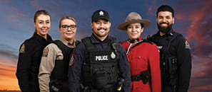 A correctional officer, conservation officer, police officer, RCMP officer and Highway patrol officer stand in front of colourful sky at dusk.