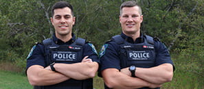 Two officers with the Saskatchewan Marshals Service stand smiling towards the camera with their arms crossed.
