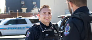 A uniformed Regina Police Service member smiling at another member with a police vehicle in the background