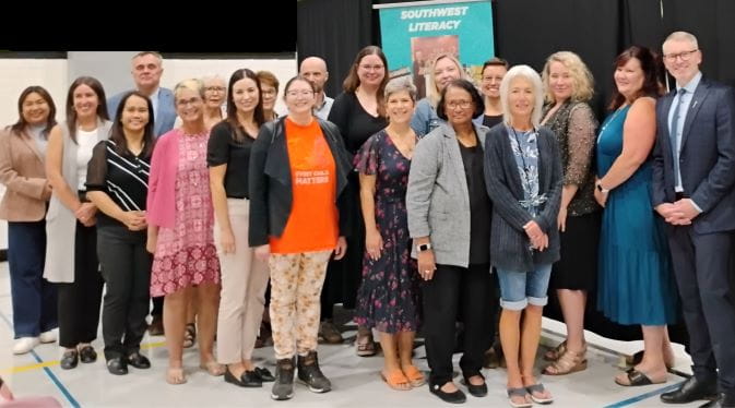 19 people including Minister of Education Everrett Hindley are standing together smiling at the camera. The group image features everyone who is a part of the Southwest Literacy Committee.
