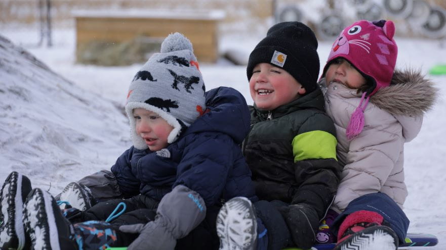Children bundled in winter gear sit together on a sled, ready for outdoor fun in the snow.