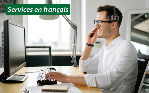 Services en francais. Smiling worker at a computer wearing a headset.