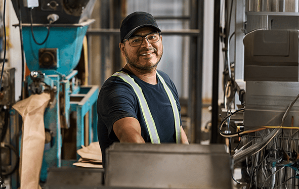 A man in a safety vest works in a factory, surrounded by industrial machinery.