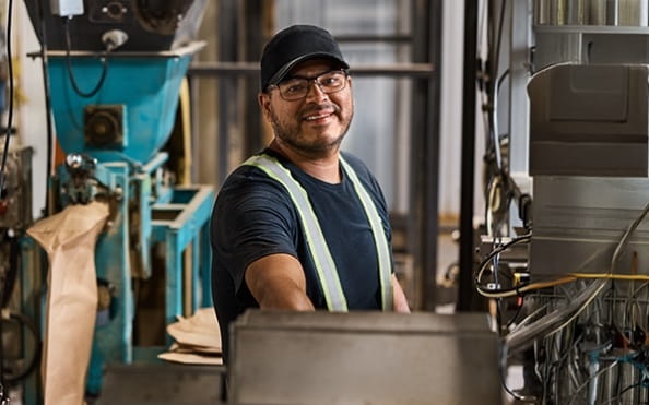 A man in a safety vest works in a factory, surrounded by industrial machinery.
