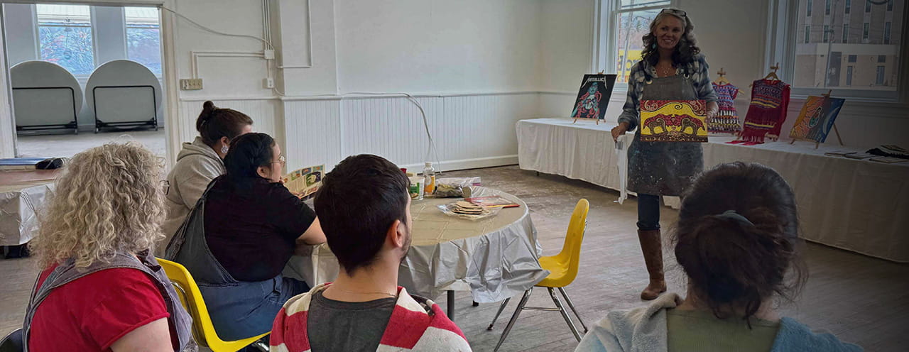 A woman shows a piece of art to a group of people sitting in chairs.