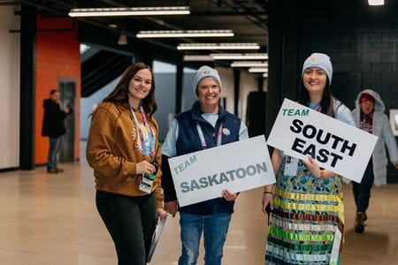 Three volunteers standing with signs cheered on the athletes from Team Southeast and Team Saskatoon who were part of the 2026 Saskatchewan Winter Games.