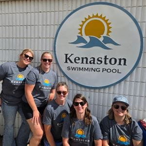 Five volunteers with the Kenaston Swimming Pool Board posing in front of the pool sign.