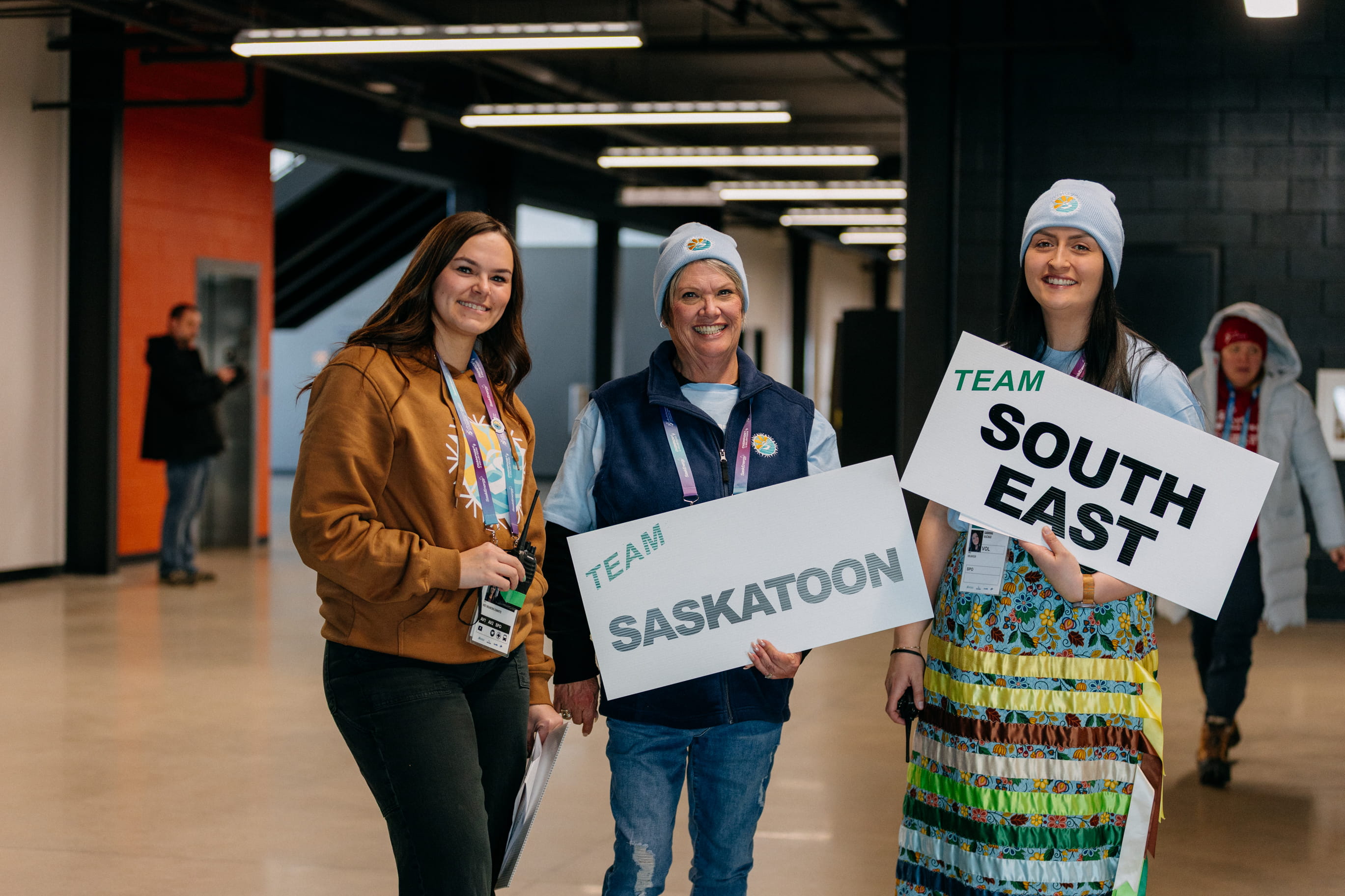 Three volunteers standing with signs cheered on the athletes from Team Southeast and Team Saskatoon who were part of the 2026 Saskatchewan Winter Games.
