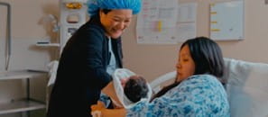 Dr. Yen, an Obstetrician-Gynecologist in North Battleford, handing newborn baby to mother