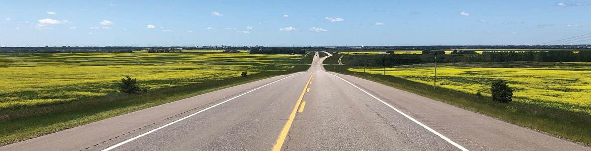 Two lane highway with canola fields on the right and left sides.