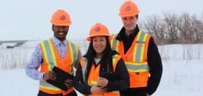 Three individuals in orange hard hats and high-visibility vests