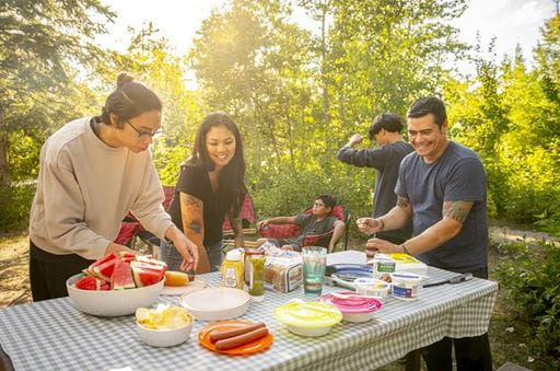 A smiling family serves up food from around a picnic table at Good Spirit Lake Provincial Park.