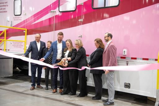 Health Minister Jeremy Cockrill joined by representatives from the Saskatchewan Cancer Agency, Cancer Foundation of Saskatchewan, Kinsmen Foundation and the Saskatchewan Health Authority to showcase Saskatchewan’s new white and pink breast cancer screening mammography semi-trailer unit preparing to cut a large pink ribbon draped in front of them. 