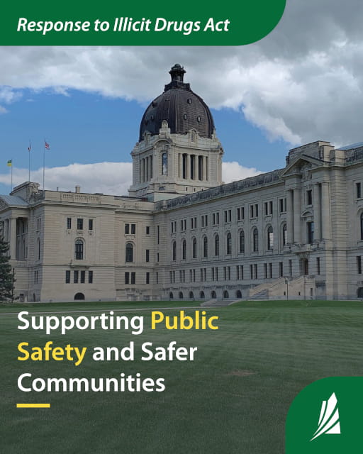 Titled ?Saskatchewan Introduces The Response to Illicit Drugs Act to Strengthen Public Safety and Support Safer Communities, the artwork features a summer view of the Saskatchewan Legislative Building in Regina, seen from across Wascana Lake, from the northeastern side. The beige stone building shows a large shiny copper dome with three flagpoles, including the Saskatchewan and Canadian flags. The building is surrounded by dense green trees that reflect in the water of the lake. A few parked vehicles and people walking along the lakeside path are visible under the bright blue sky.
