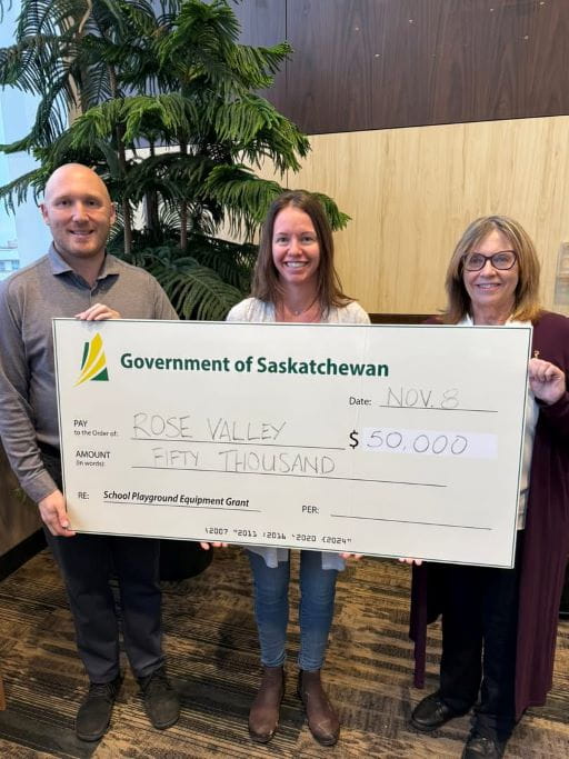 Three people holding a large white cheque for the School Playground Equipment Grant program for Rose Valley Schools for $50,000. The big cheque has the green and yellow Government of Saskatchewan logo on it. 