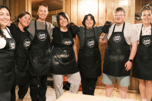 A group of seven people stand wearing Field to Shield aprons. Chef Jenni Lessard stands in the middle, wearing black oven mitts with red accents. Field to Shield by Adventure Destinations won the Culinary Tourism Experience award at the Canadian Tourism Awards on Thursday, Nov. 20, 2025.