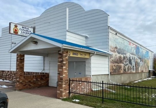 Exterior of the Legion Branch 120 in Nipawin. The building is next to a fenced park with a mural on the building side depicting the D-Day landings. 