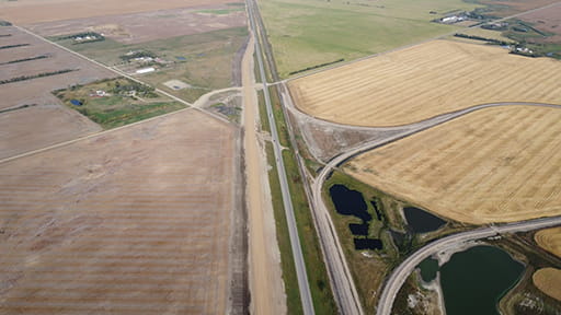 Aerial view of Highway 39 twinning near Weyburn. An existing set of lanes with black pavement is near a set of new lanes under construction that have sand and gravel on them.