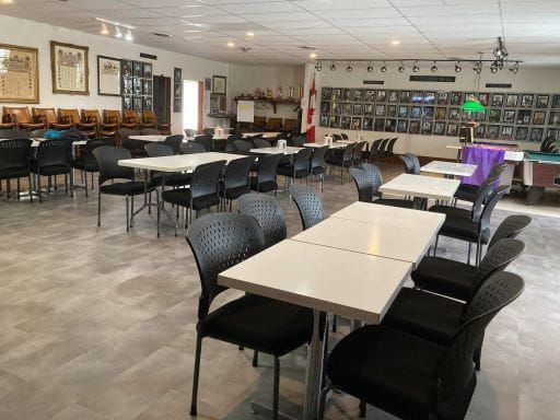 Image is of the Stoughton Legion Branch 133 lounge. There are rows of tables with black chairs and in the background is a pool table. The application period for the 2026-27 Saskatchewan Veterans Service Club Support Program has opened and runs until May 15, 2026.