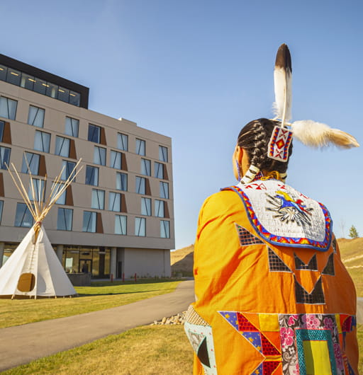 A woman, wearing traditional Indigenous regalia, is standing and viewing a tipi which is placed in front of the Dakota Dunes Hotel. Dakota Dunes Resort is a finalist at the 2026 Indigenous Tourism Awards, which will be held in Edmonton on February 19, 2026.