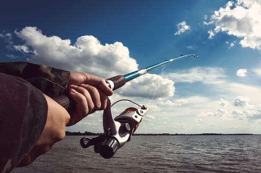 A man with his fishing rod pointed out over the water as he fishes